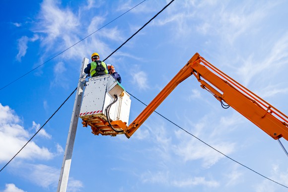 An aerial lift being used to lift a worker installing distribution lines.