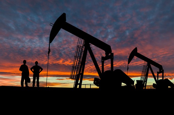 Oil workers standing next to an oil rig at sunset.