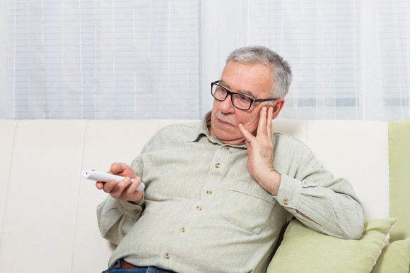 Bespectacled older man holding a remote control, looking bored