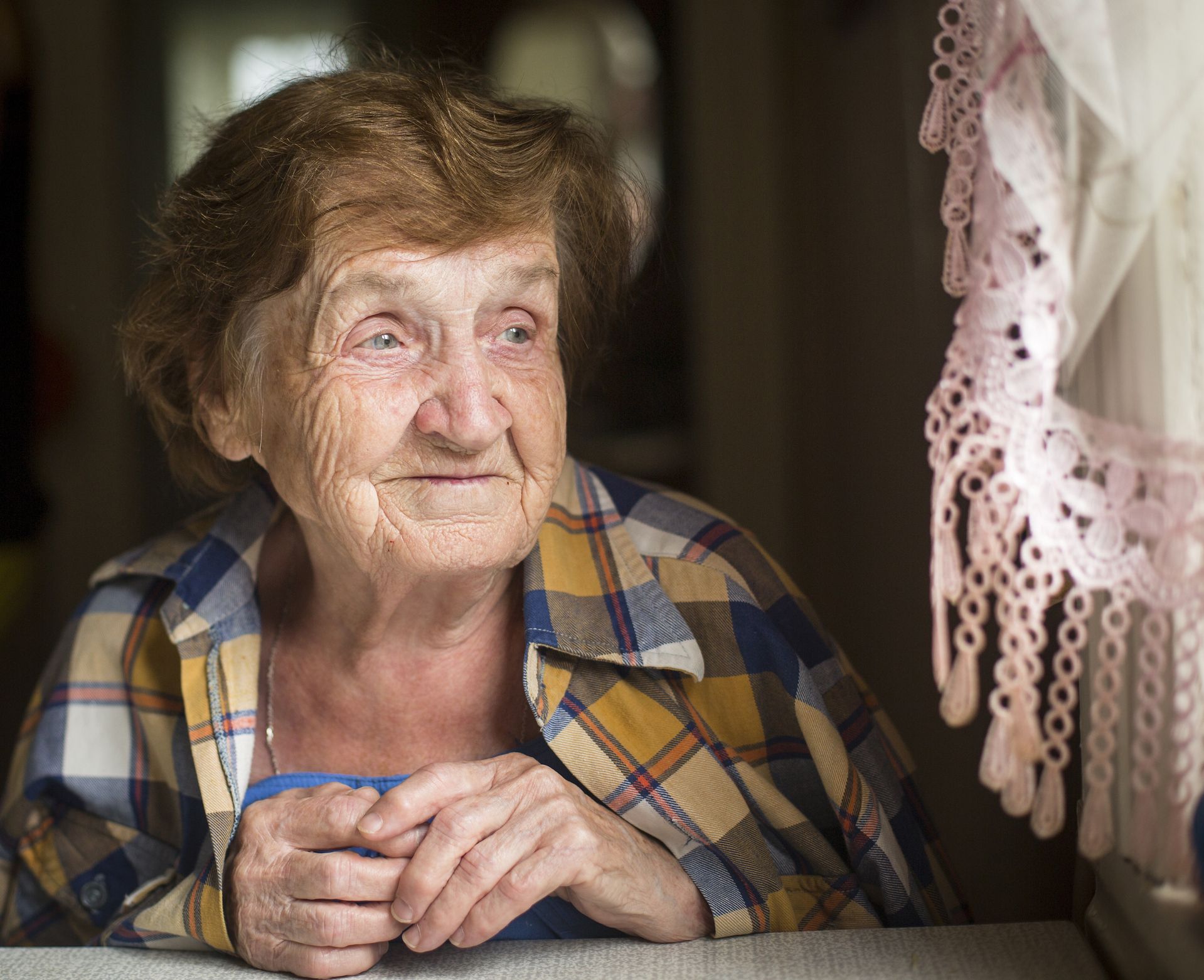 Smiling elderly woman sitting at her table and looking out the window