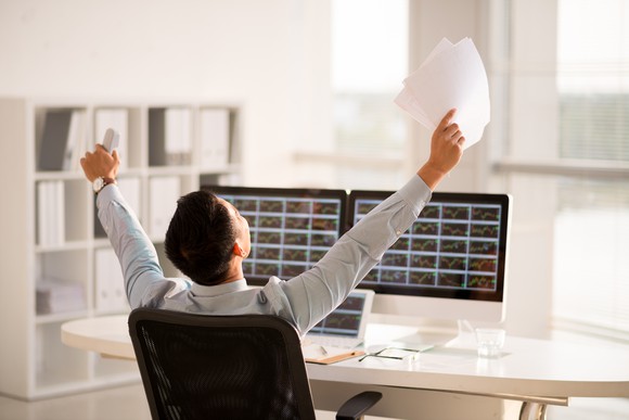 An investor celebrating in front of a computer screen.