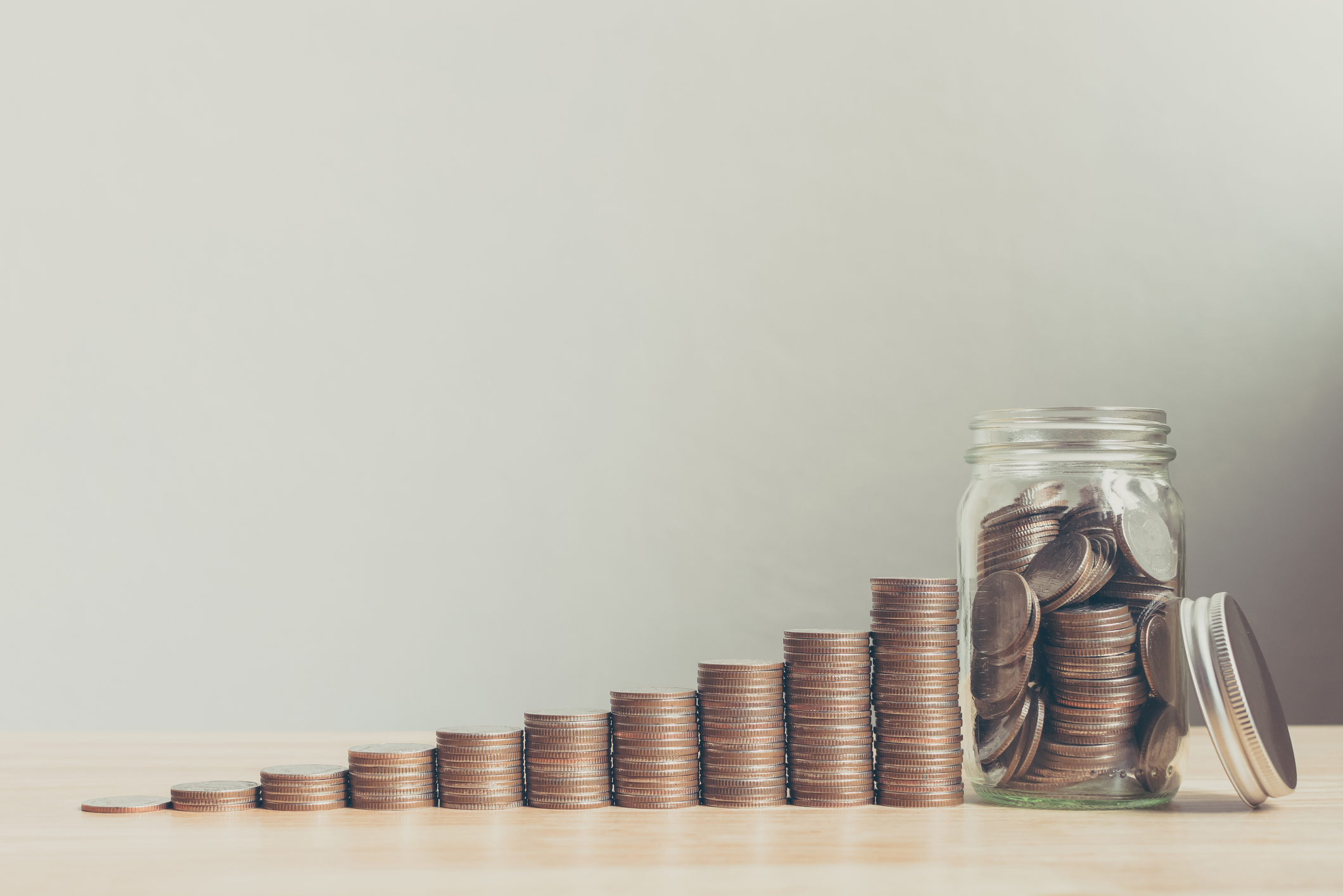 Piles of coins growing increasingly larger, ending in a full jar.