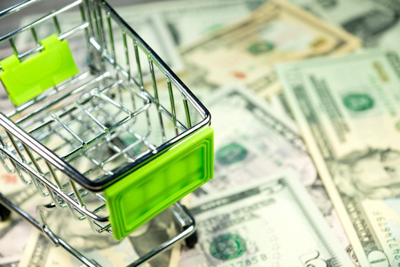 Little shopping cart being pushed over dollar bills.