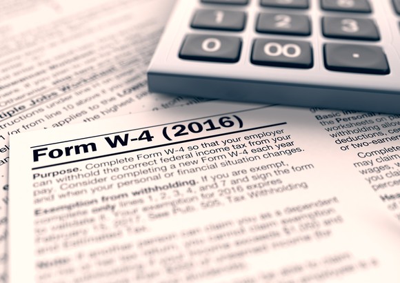 Form W-4 federal tax withholding form sitting next to a calculator.