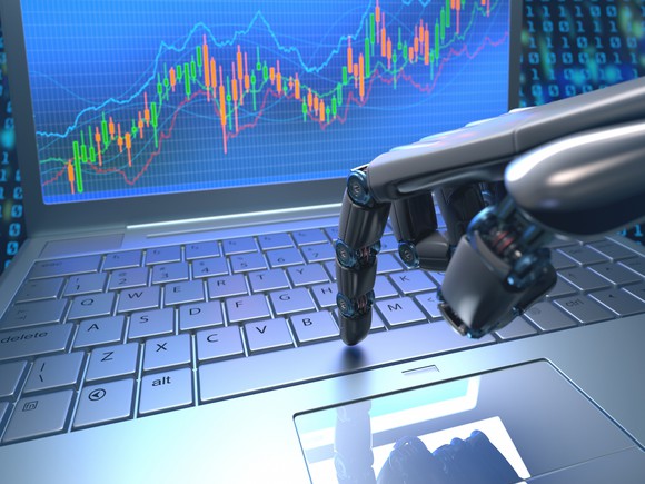 The hand of a robot clicking keys on a laptop with a stock chart on the screen.