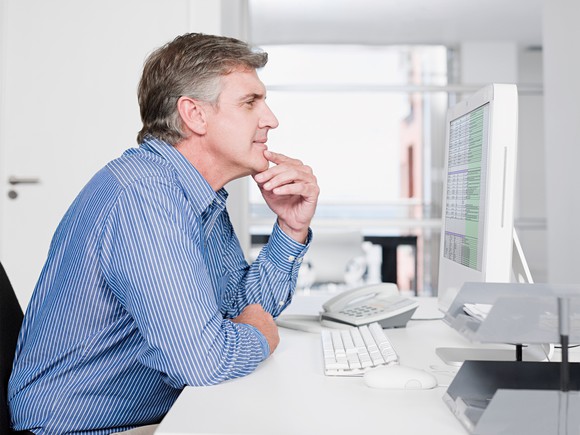 Middle-aged man at desk thinking in front of a computer screen