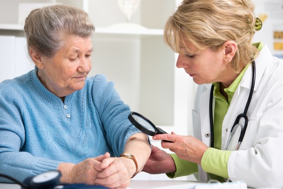 Dermatologist examining skin of an elderly patient.