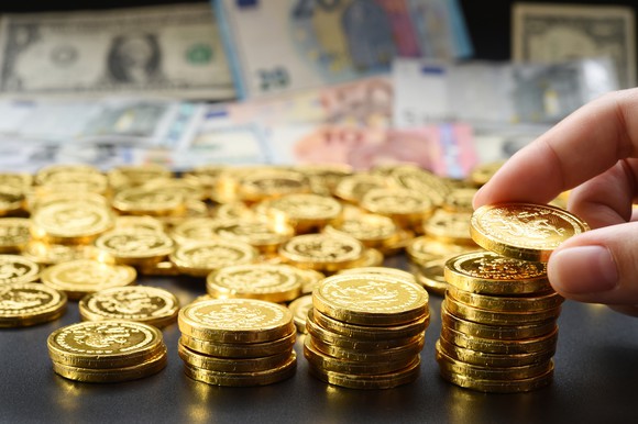 A hand stacks gold coins.