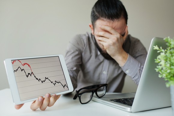 Stock trader with his face buried in his hand while holding up a declining stock chart.