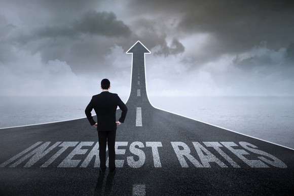 Businessman contemplating a highway labeled "interest rates" that rises on the horizon.