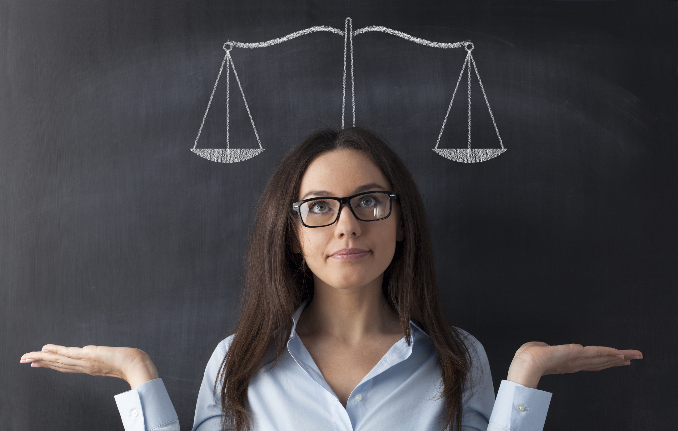 Woman weighing a decision in front a chalk board with a scale drawn on it.