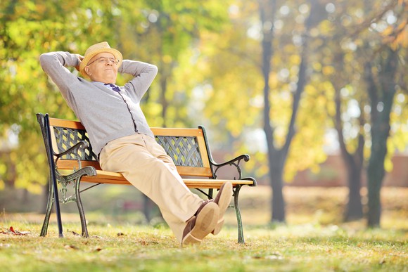 Man on park bench, arms clasped behind his head, happy