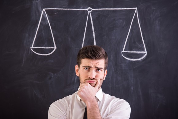 Man thinking about decision with scales drawn on chalkboard