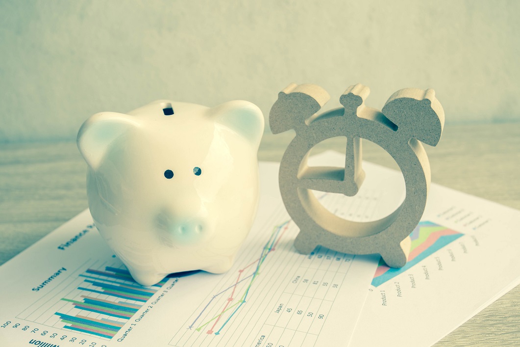 Piggy bank and wood clock cutout on top of investment paperwork.
