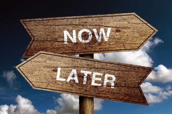 Two intersecting signs -- one says now, one says later