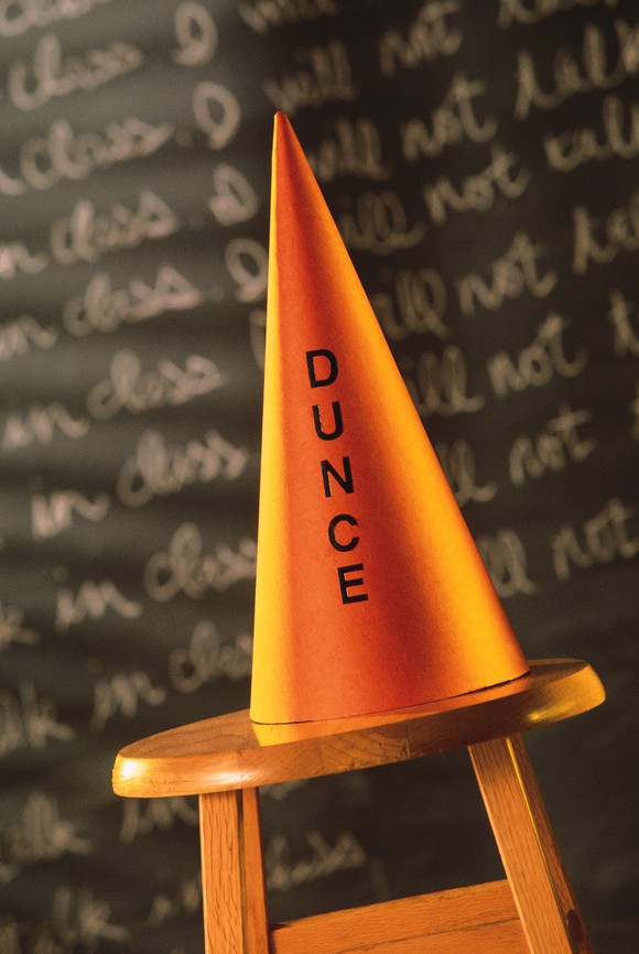 Dunce cap on a stool in front of a blackboard