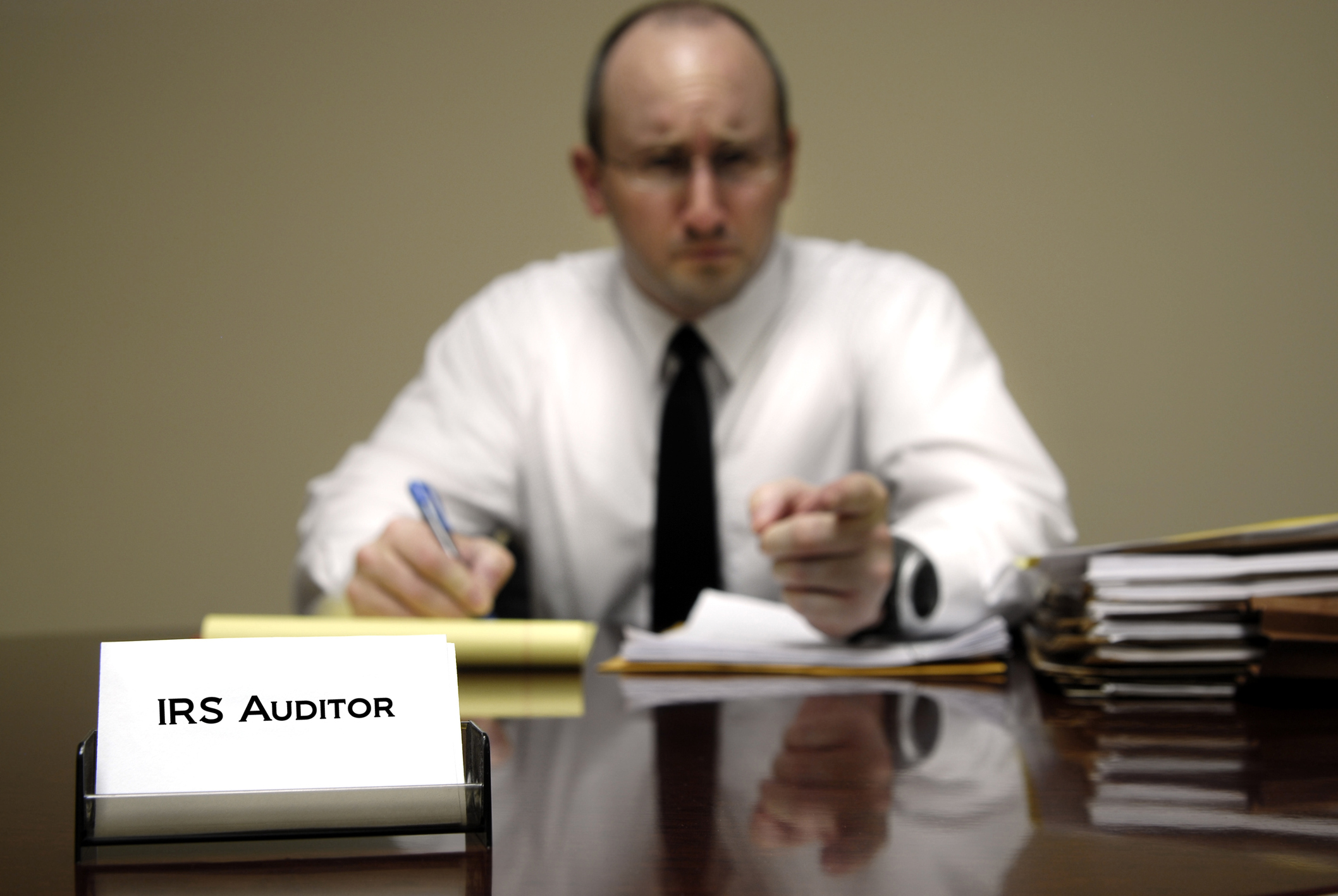 IRS employee at desk with nameplate that says "IRS auditor," looking mad and pointing at viewer
