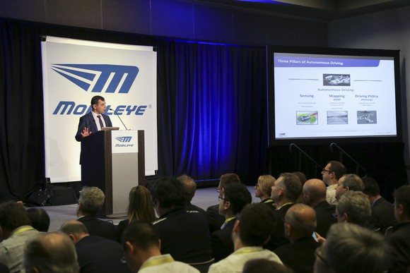 Amnon Shashua at a podium, next to a slide outlining Mobileye's self-driving effort