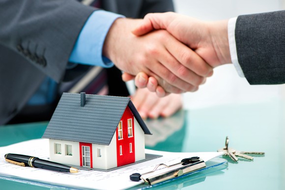 Shaking hands over a contract and a miniature house