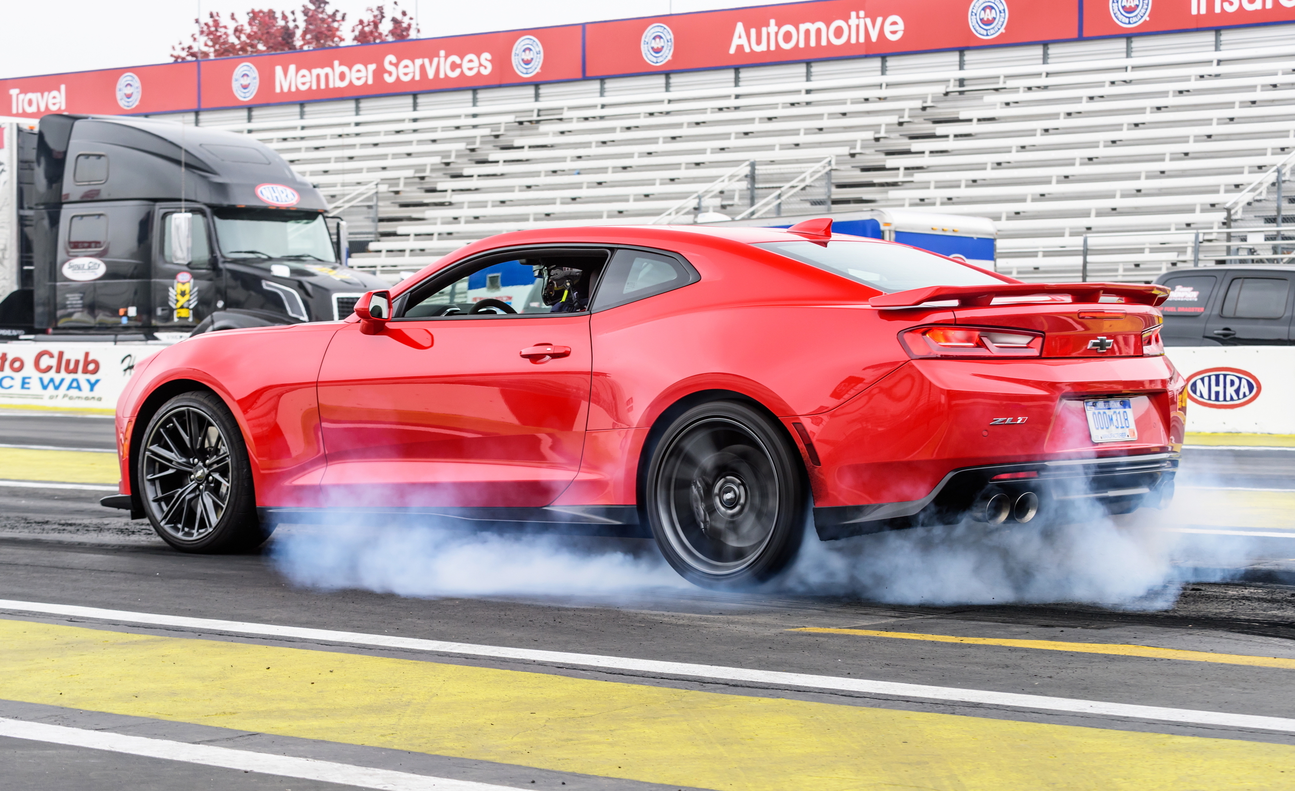 A red Chevrolet Camaro burning rubber on a drag strip.