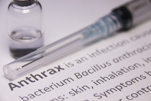 A vial and needle sitting on a paper with a description of anthrax.