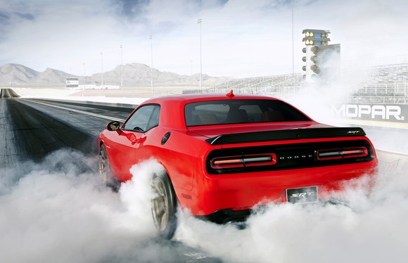 A red Dodge Challenger SRT Hellcat burning rubber on a drag strip.