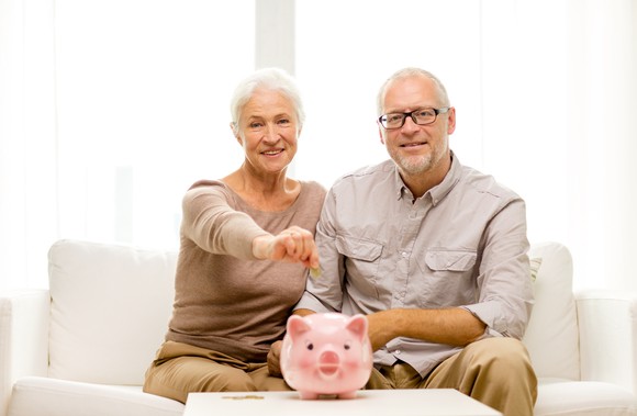 Senior couple smiling, with a pink piggy bank