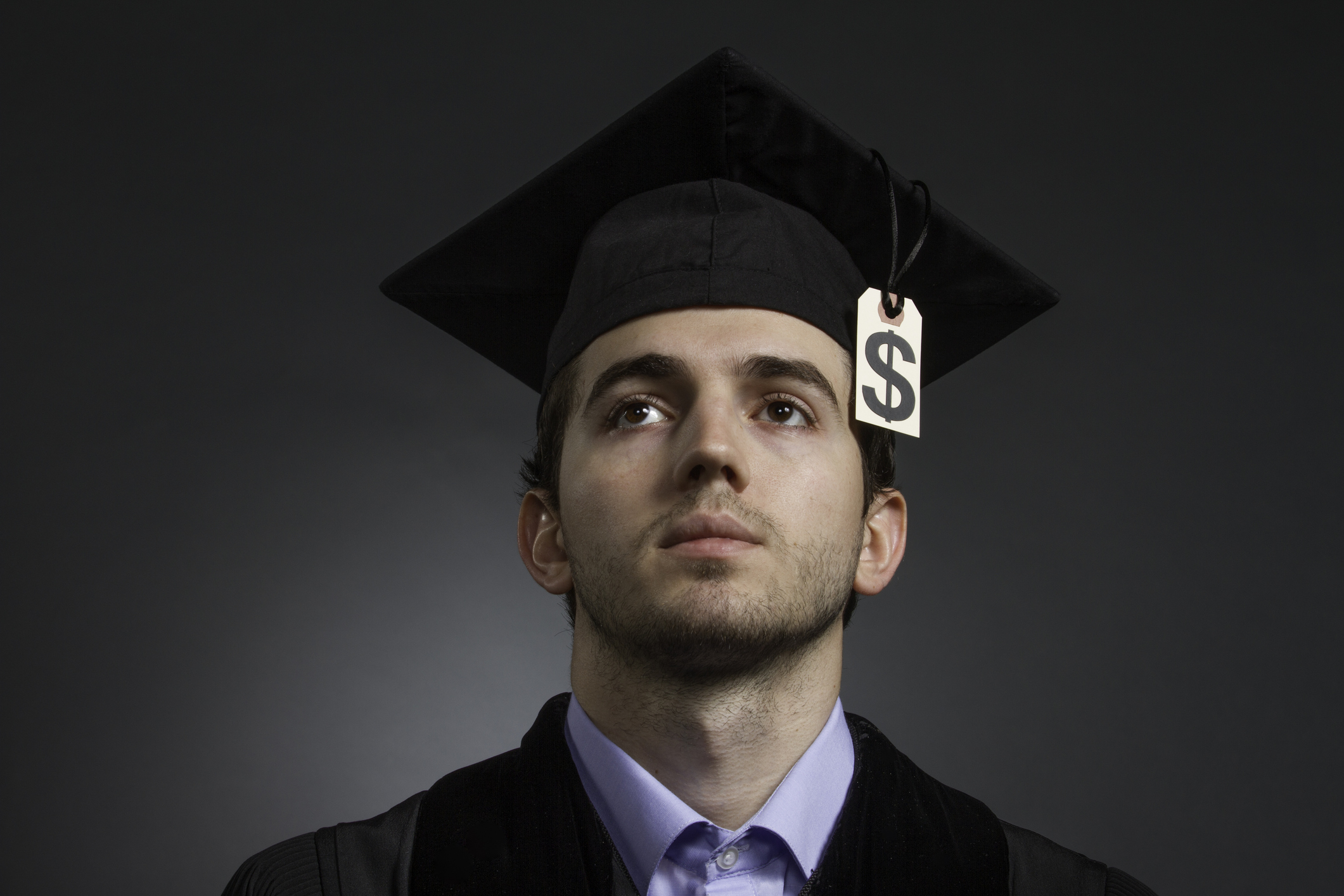 College student wearing a cap and gown with a dollar sign at the end of the tassel.
