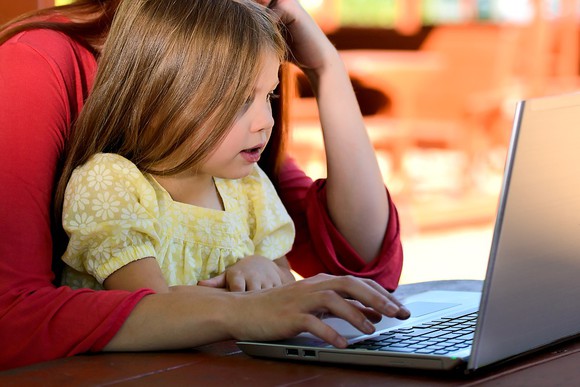 Child on parent's lap in front of laptop.