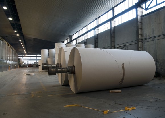 A roll of newly manufactured paper sitting on the floor of an industrial pulp and paper mill.
