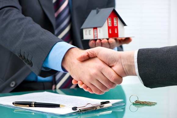 Two people signing mortgage paperwork and metaphorically handing over a house.