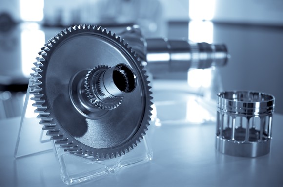 Image of a precision gear and other parts in the background.
