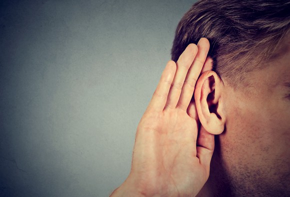 A man cups his ear as if ready to hear something.