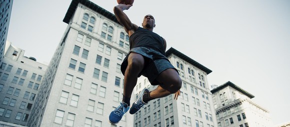 A basketball player wearing Nike shoes jumps over the camera about to dunk the ball.
