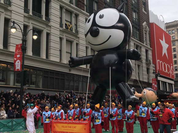 A Macy's Day Parade balloon passes by a Macy's store.