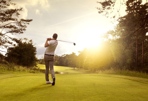 Man teeing off on golf course at sunrise.