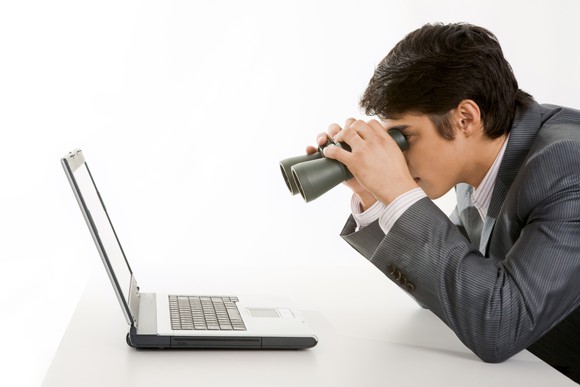 Businessman looking at computer with binoculars