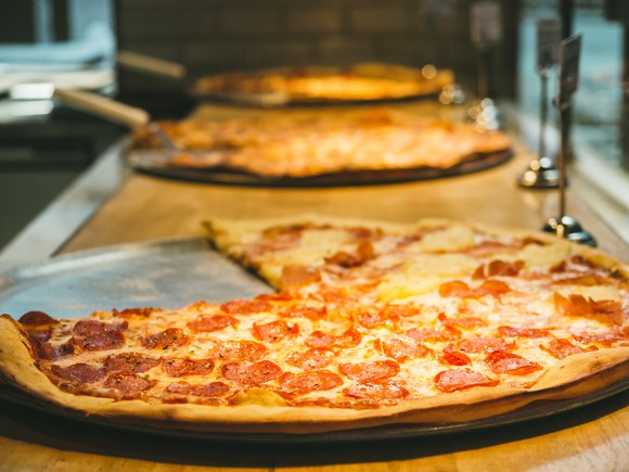 Three pizzas warming under a heater.