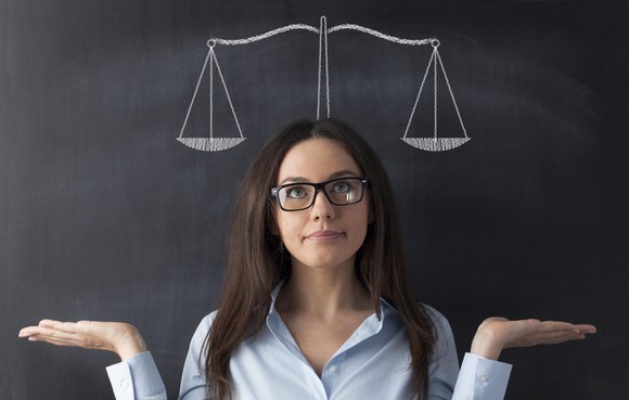 A person pretending to weigh two options in front of chalkboard with a picture of a scale.