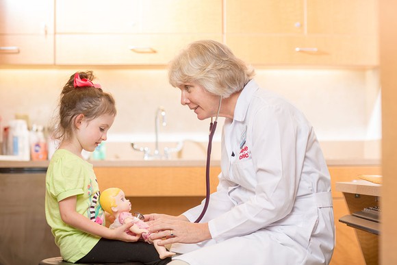 A doctor with her stethoscope interacting with a young patient.