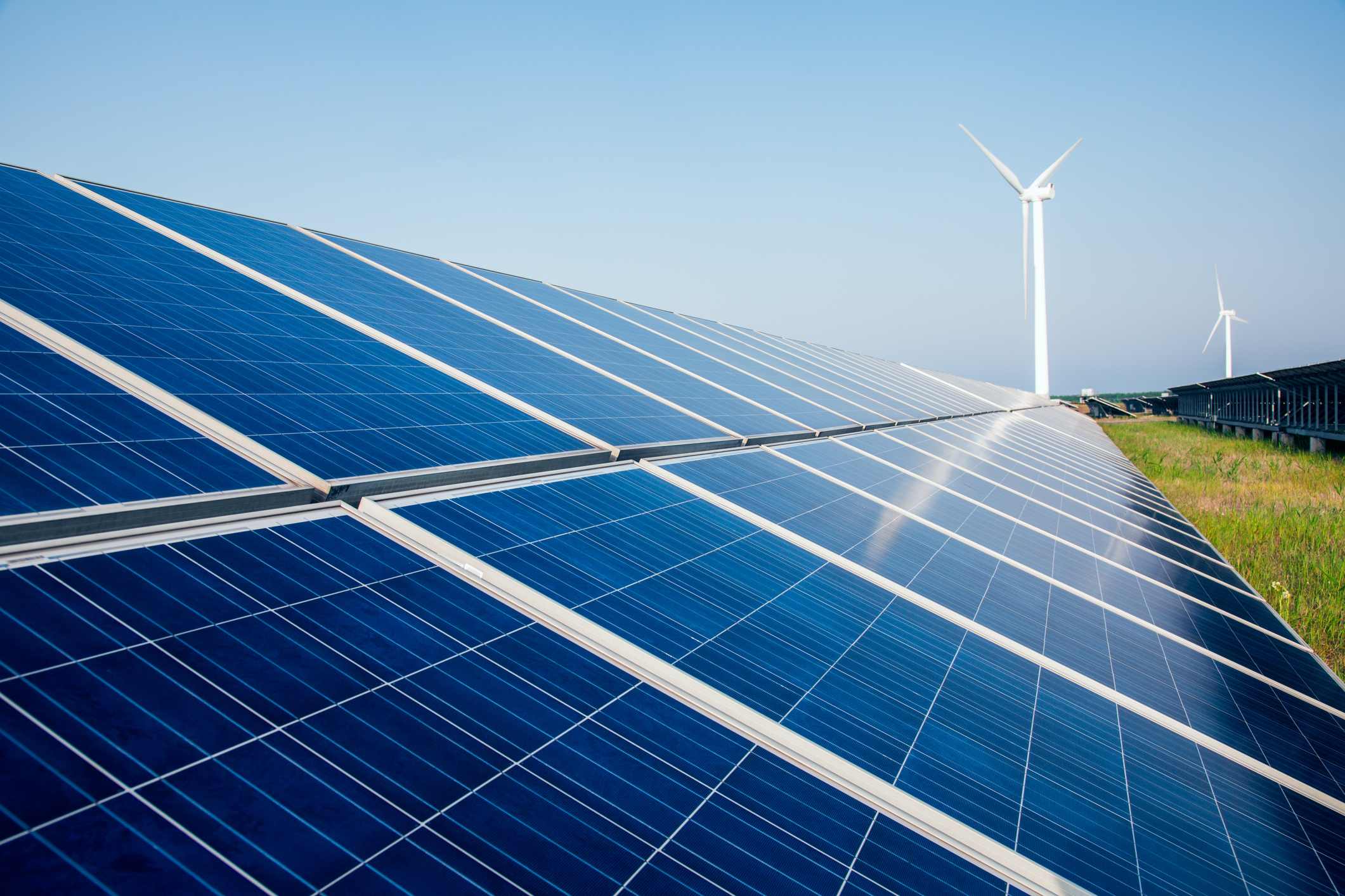 Solar panels of a solar farm with a wind turbine in the background.