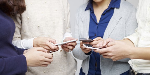 A group of people stand in a circle, all typing on their smart phones.