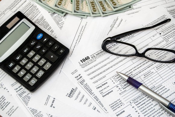 Tax forms with calculator, glasses, pen, and money.
