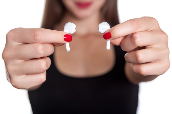 Woman holding up two wireless earbuds.