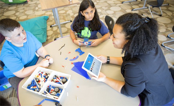 A woman demonstrates Watson's AI capabilities to two children.