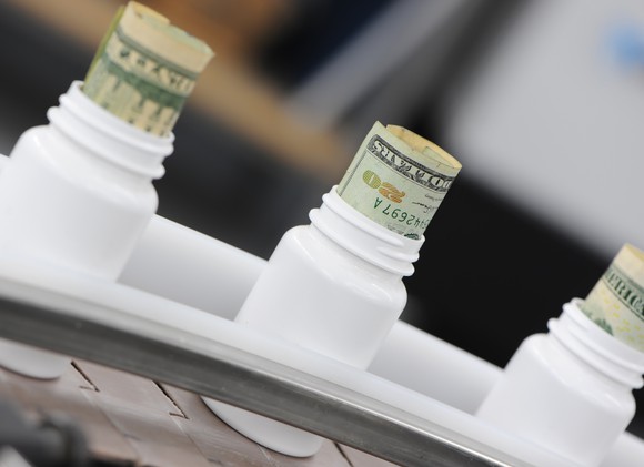 Pill bottles on a drug manufacturing line with cash sticking out the top of the bottles.