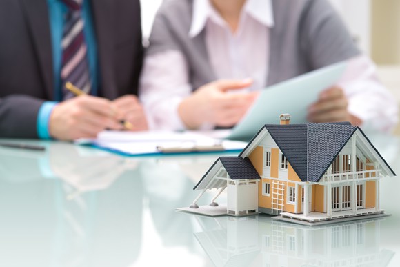 Two people signing documents, behind a model of a house on a table.
