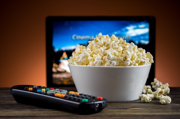 A bowl of popcorn and a TV remote in front of a TV.