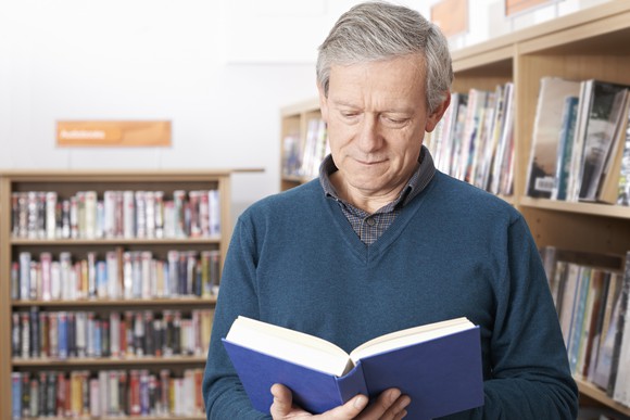 Senior man reading a book in a library