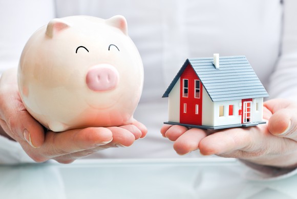 Hands holding piggy bank and house model.